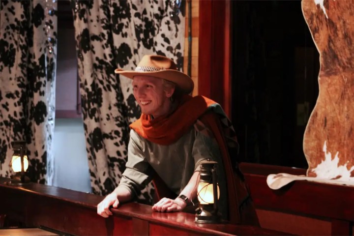 Person in cowboy hat smiling at wooden counter with lanterns, cow print curtains.