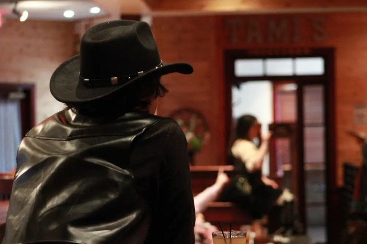Man in black hat and jacket at a bar, facing away.